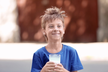 Cute boy in blue shirt holding glass of milk on blurred background