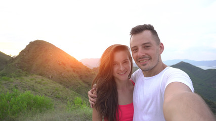 Young couple taking selfie, laughing and go round in the mountains with beautiful aerial city view at sunset, enjoy the nature and carefree life