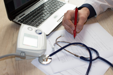 Doctor working at table in office. Hands of a doctor filling RX prescription, documents at the desk