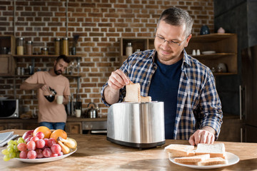 Smiling man in eyeglasses preparing toasts while bearded man pouring coffee behind