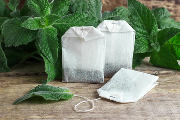 White packages of disposable tea with mint branches on a wooden background