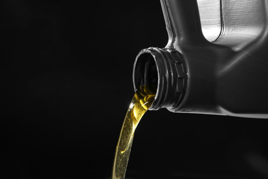 Engine oil pouring from canister on dark background, closeup