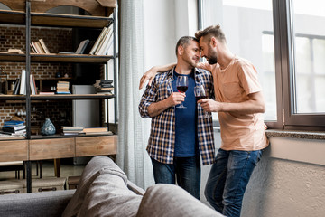 casual homosexual couple able to kiss while holding wine glasses at home