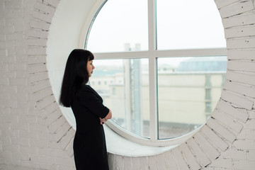 A girl in a black dress is standing in front of a big window in the office