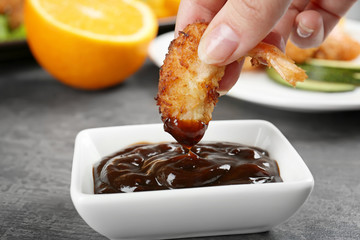 Female hand dipping delicious coconut shrimp in sauce, closeup