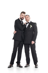 homosexual couple of grooms in tuxedos embracing while standing together isolated on white