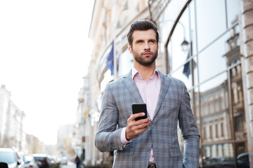 Handsome man in a jacket walking and holding mobile phone