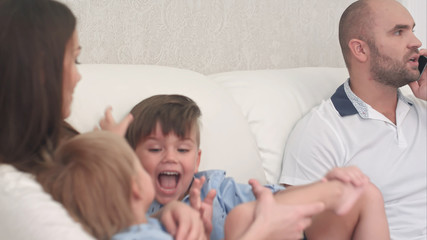 Obraz premium Father talking on the phone while little boys playing with their mother on the sofa