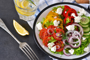 Vegetable mix salad with feta cheese on a black slate background.