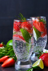Summer drink. Cold lemonade with lime, rosemary and strawberries in a black, marble background.