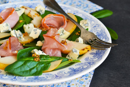 Salad with spinach, blue cheese, ham and pear sauce on a concrete background