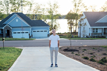 Fototapeta na wymiar Attractive american teenager in grey sweatpants and white tshirt walks the driveway to a typical residential home, on warm summer evening with soft sunset light
