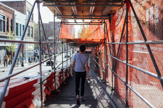 Silhouette of young hipster man with fashionable and stylish haircut, walking down busy street with scaffolding, in warm summer light and beautiful shadows
