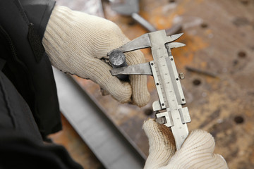 Man using vernier caliper for measuring metal bar in shop