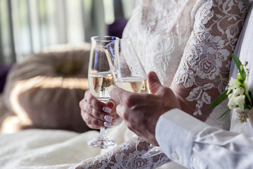 The bride and groom with glasses of champagne are sitting on the sofa in the hotel room