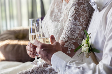 The bride and groom with glasses of champagne are sitting on the sofa in the hotel room