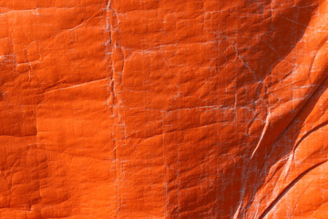 Orange color plastic tarpaulin covering, polyester fabric texture.