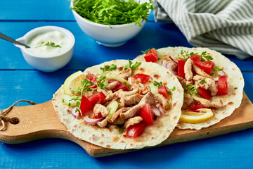 Grilled chicken and fresh vegetables salad tortilla on a blue wooden background .Healthy delicious breakfast or snack. Flat lay.Outdoors Food Concept