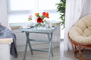 Vase with beautiful flowers and tea set on table in modern veranda interior