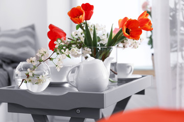 Vase with beautiful flowers and tea set on table in modern veranda interior