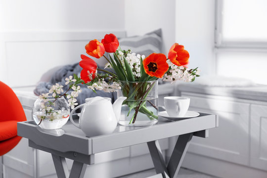 Vase with beautiful flowers and tea set on table in modern veranda interior