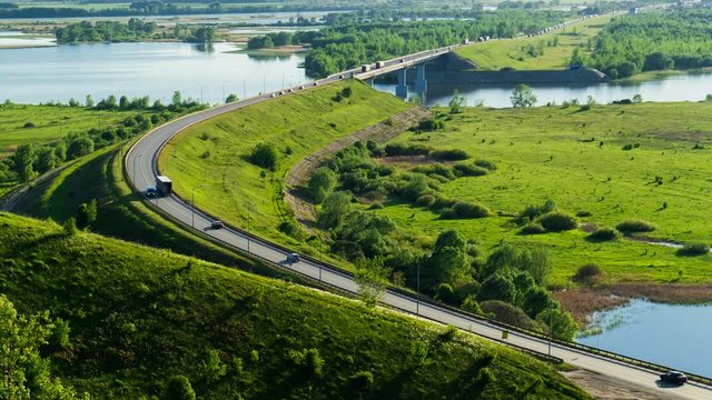 A large number of trucks and cars driving on long bridge road, among the forests, fields and rivers. Timelapse