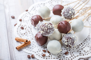 Fototapeta na wymiar Cake pops decorated with white, dark chocolate and coconut on napkin, natural light selective focus