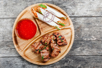Grilled pork and vegetables with fresh salad and bbq sauce on cutting board on wooden background close up. Hot Meat Dishes. Top view