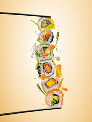 Sushi pieces placed between chopsticks, separated on colored background. Popular sushi food. Flying rice above.