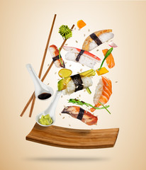 Flying sushi pieces served on wooden plate, separated on colored background. Many kinds of popular sushi food with chopsticks. Concept of flying asian dish with ingredients