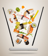 Flying sushi pieces served on plate, separated on colored background. Many kinds of popular sushi food with chopsticks. Concept of flying asian dish with ingredients