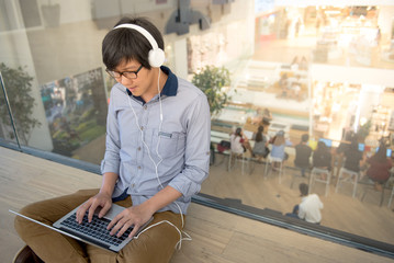 Young Asian man dressed in casual style using laptop computer while listening to music. Digital...