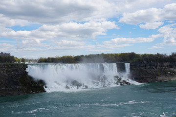 Niagara Falls waterfall on bright spring day with clouds and blue sky as seen from Ontario, Canada