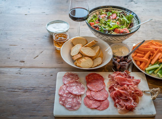 Wine appetizer set. Glass of red wine, baguette, olives, smoked meat, salad and salami on a rustic wooden table.