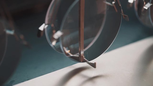 Newly made glass lenses swing on metal brass conveyor fastening at factory, close up