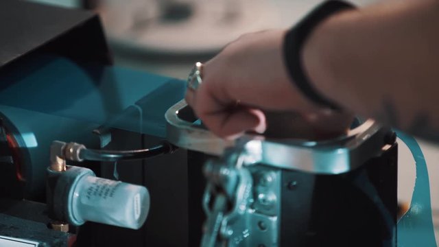 Lens manufacturer. Man hands with fitness tracker, rings and tattoo put blue film on lens using packing machine