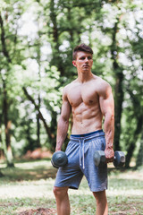 Young muscular man posing with weights outdoors