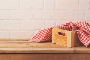 Empty wooden deck table with box and tablecloth over brick wall background