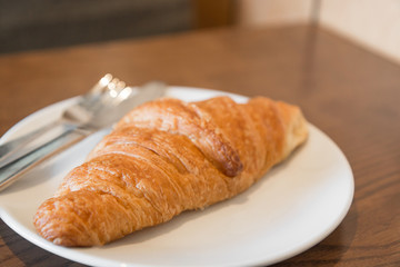 Warm fresh Croissants on a white plate with fork and knife in the coffee shop.(Selective focus with shallow depth of field)