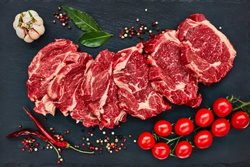 Washable wall murals Meat Fresh raw beef steaks with pepper and tomatoes on black slate board. Copy space, top view. 
