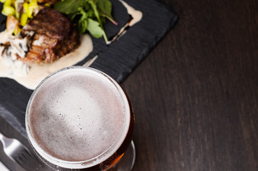 Beer glass and steak on black table, view from above.