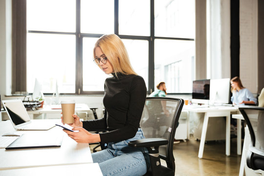 Woman work in office using mobile phone drinking coffee