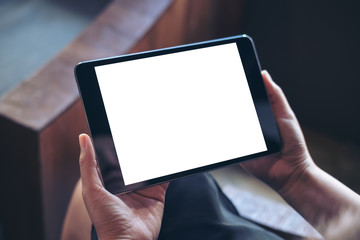 Mockup image of woman's hand holding black tablet pc with blank white screen in wooden cafe