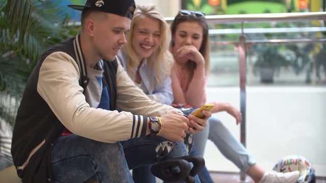 Guy sends a message from a mobile phone. Group of friends of teenagers in a modern shopping center