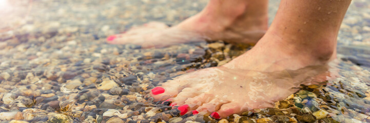 Feet with red nails on a stony beach