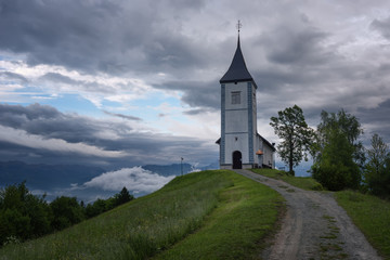 Fototapeta na wymiar Jamnik church on a hillside in the spring, foggy weather at sunset in Slovenia, Europe. Mountain landscape shortly after spring rain. Slovenian Alps. 
