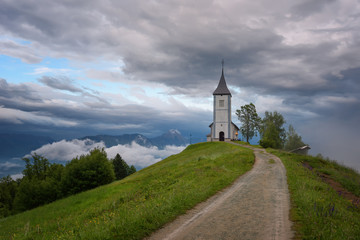 Jamnik church on a hillside in the spring, foggy weather at sunset in Slovenia, Europe. Mountain landscape shortly after spring rain. Slovenian Alps. 