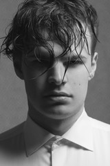 Male beauty concept. Portrait of young man with perfect haircut wearing white classic shirt. Old Hollywood star style. Wet curly hair. Close up. Monochrome studio shot
