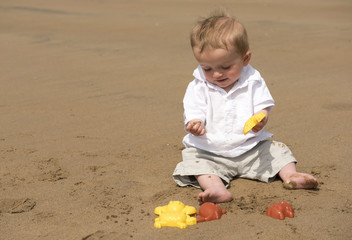 One year old baby boy playing with sand on the beach 