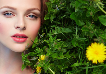 Beautiful young natural well-groomed girl lies on the grass with yellow flowers - dandelions. Natural makeup, close-up, dark light brown healthy shiny hair. Makeup is nude. Health, beauty.